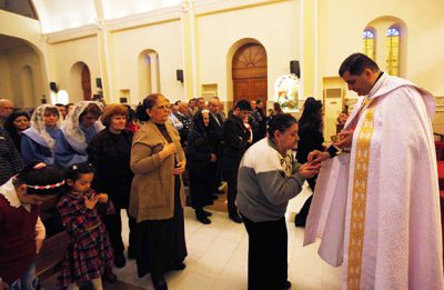 A priest gives communion to an Iraqi Christian woman, during mass at Mar George Chaldean Church in Baghdad, March 1, 2015. Iraqi Christians say they have no intention of leaving the country despite the recent abduction of over 100 Assyrian Christians by the Islamic State. Picture taken March 1, 2015. REUTERS/Ahmed Saad (IRAQ - Tags: RELIGION CIVIL UNREST) - RTR4RQVD